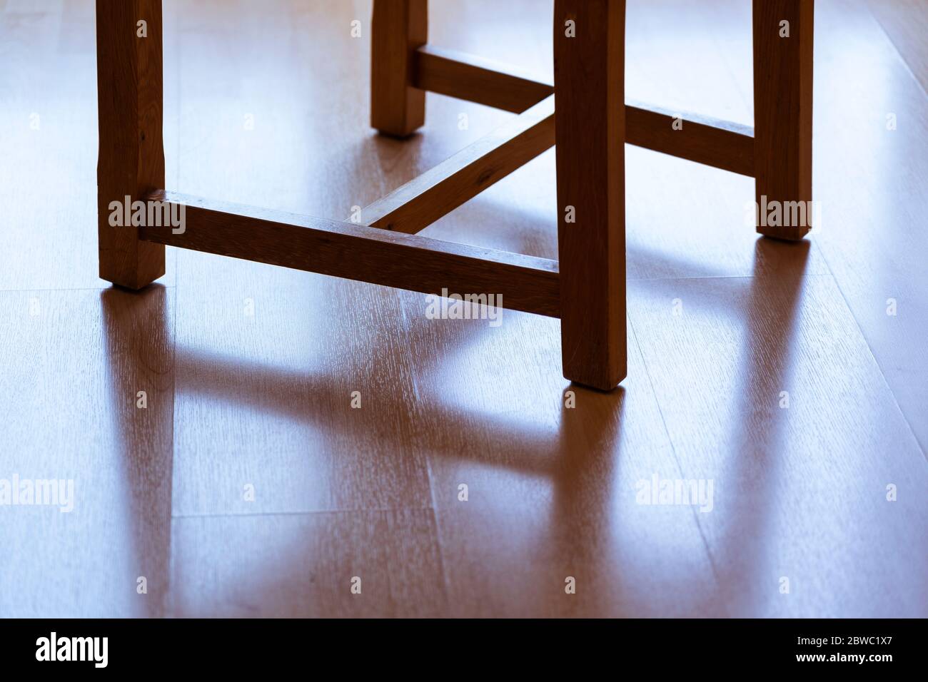 Der Schatten der Beine eines hinterleuchteten Esszimmers Holzstuhl reflektiert auf einem Laminat-Holzboden Stockfoto