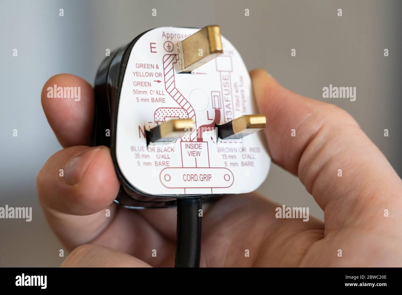 Eine Hand, die einen britischen 3-poligen Standardstecker mit Anweisungen zur Verkabelung der Erdung, des Neutralleiters und der stromführenden Kabel hält Stockfoto