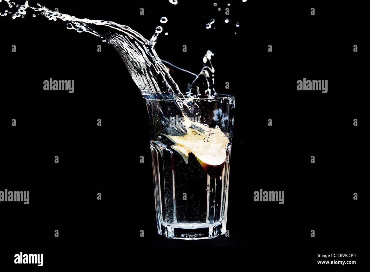 Apfel spritzt in Glas Wasser auf schwarzem Hintergrund. Transparente Flüssigkeit in Bewegung mit Tröpfchen. Erfrischendes Fruchtgetränk mit Wasser Stockfoto