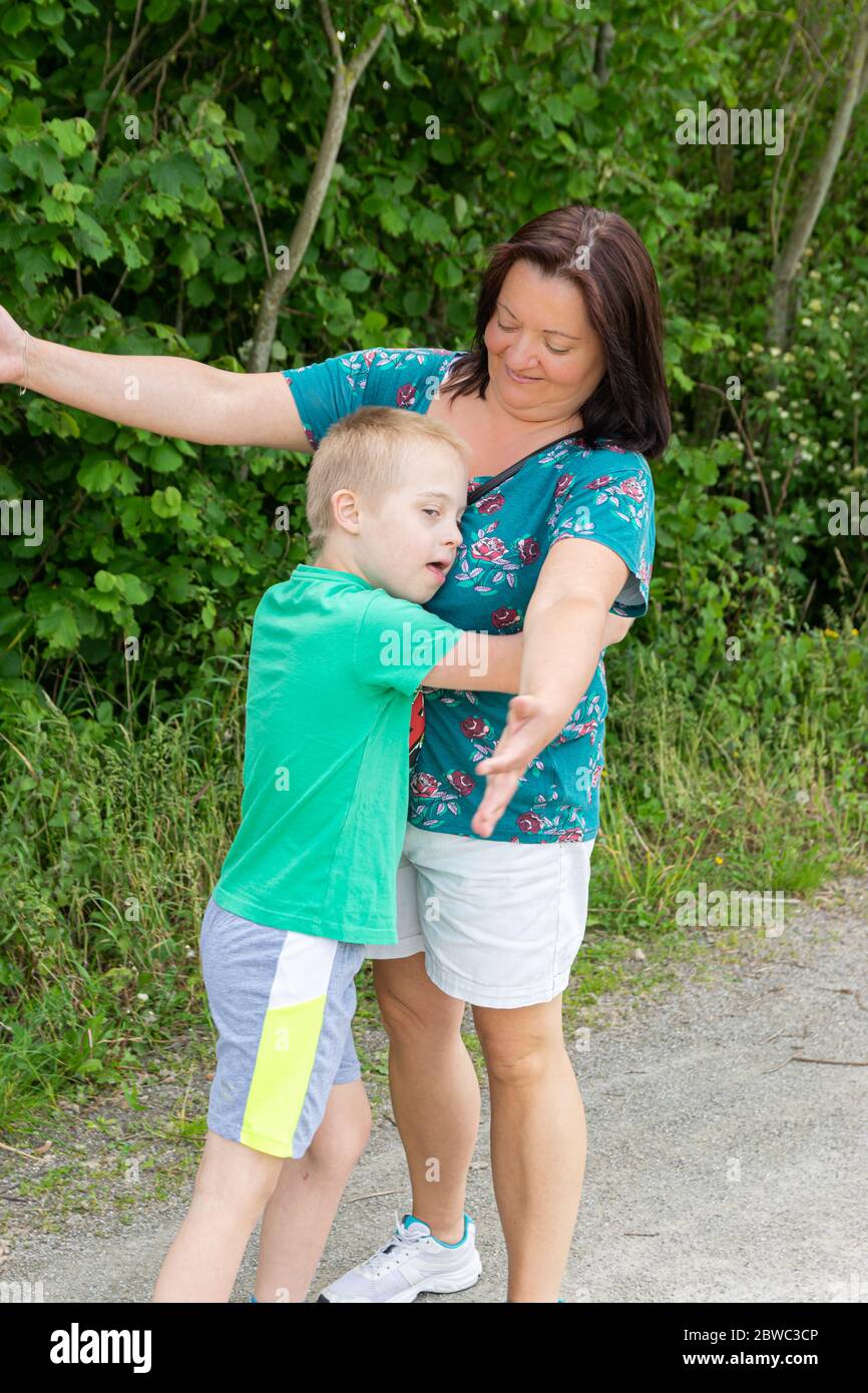 Defekt, Kinderbetreuung, Medizin und Menschen Konzept: Glückliche Mutter und Sohn mit Down-Syndrom umarmte zusammen im Park. Stockfoto