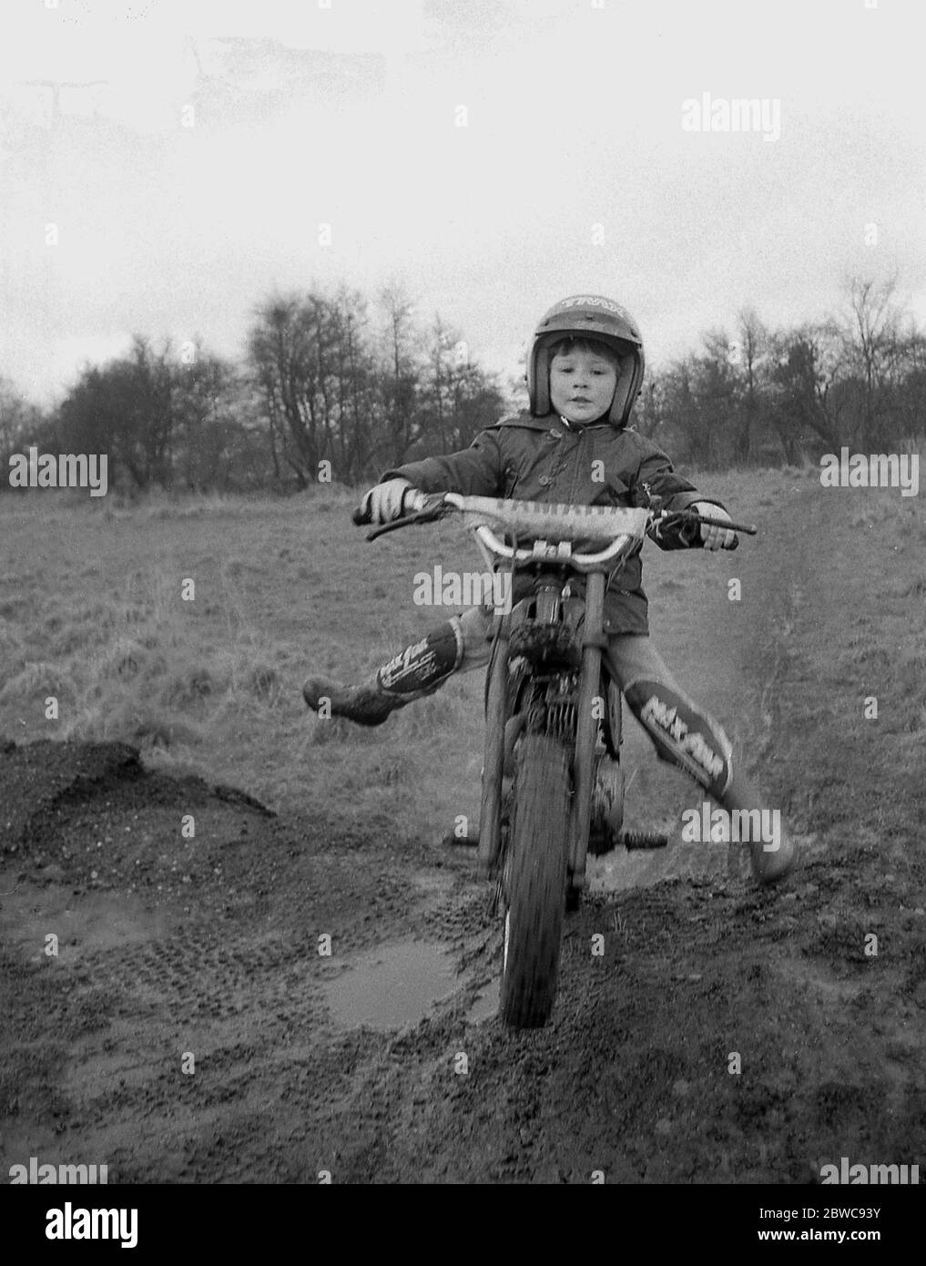 "Starting Young", ein mutiger Junge, vielleicht erst 6 Jahre alt, auf einem Motorrad-Probelauf auf einem Feld über einem Hügel auf einer feuchten schlammigen Strecke, England, Großbritannien, 1980er Jahre. Trials Reiten ist eine beliebte Teilnahme Motorradsport und junge Menschen sind ermutigt, teilzunehmen. Stockfoto