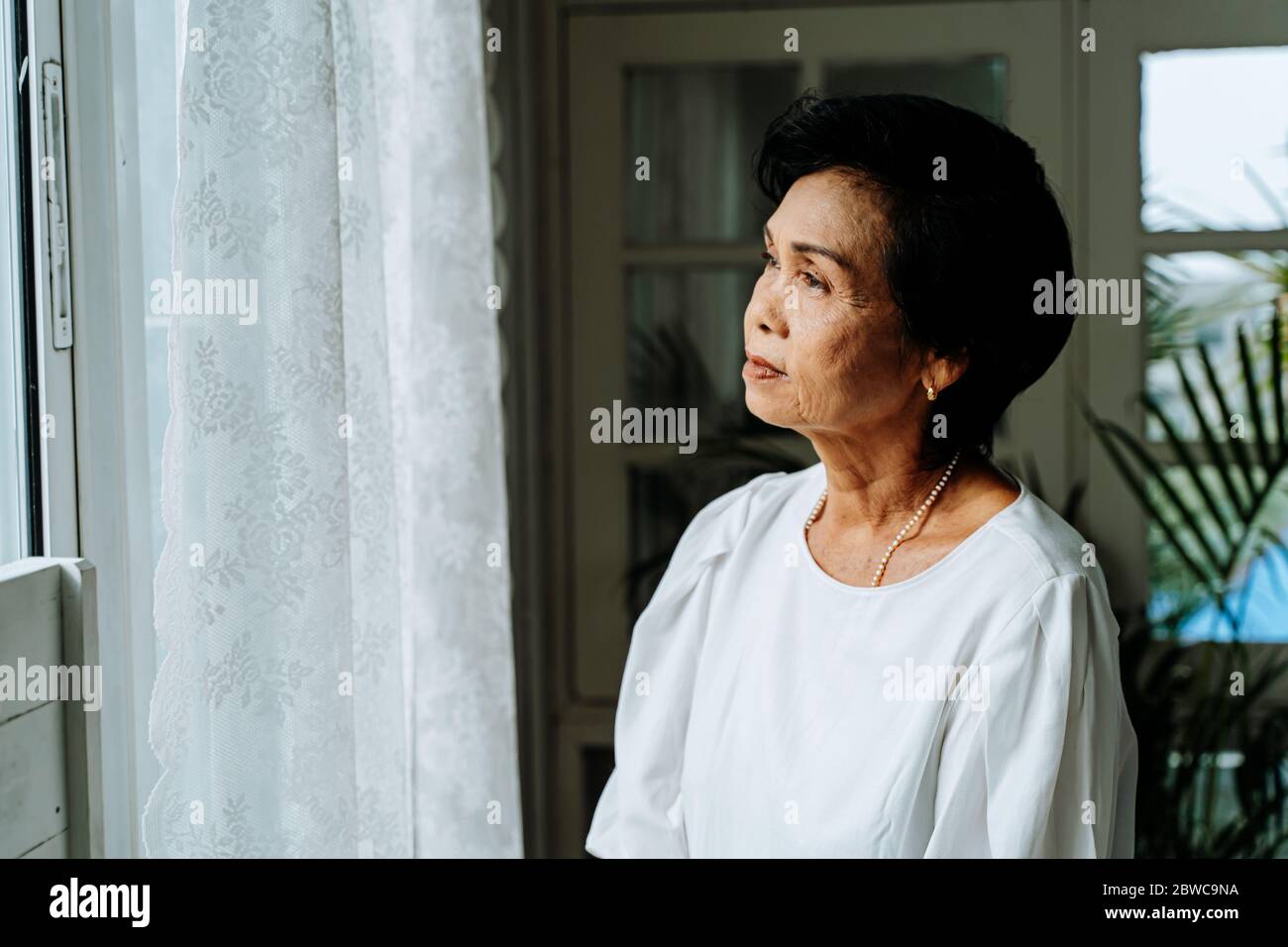 Nahaufnahme von nachdenklichen alten Frau aus dem Fenster schauen Gefühl einsam. 70er Jahre Asian ältere weibliche Rentnerin vermisst Kinder und Ehemann Stockfoto