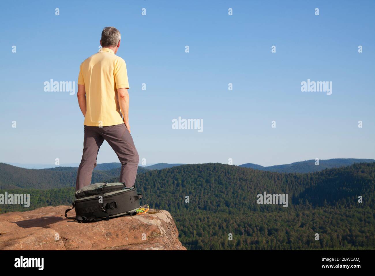 Reifer Wanderer auf einem Felsen vor Hügeln mit Wald Stockfoto