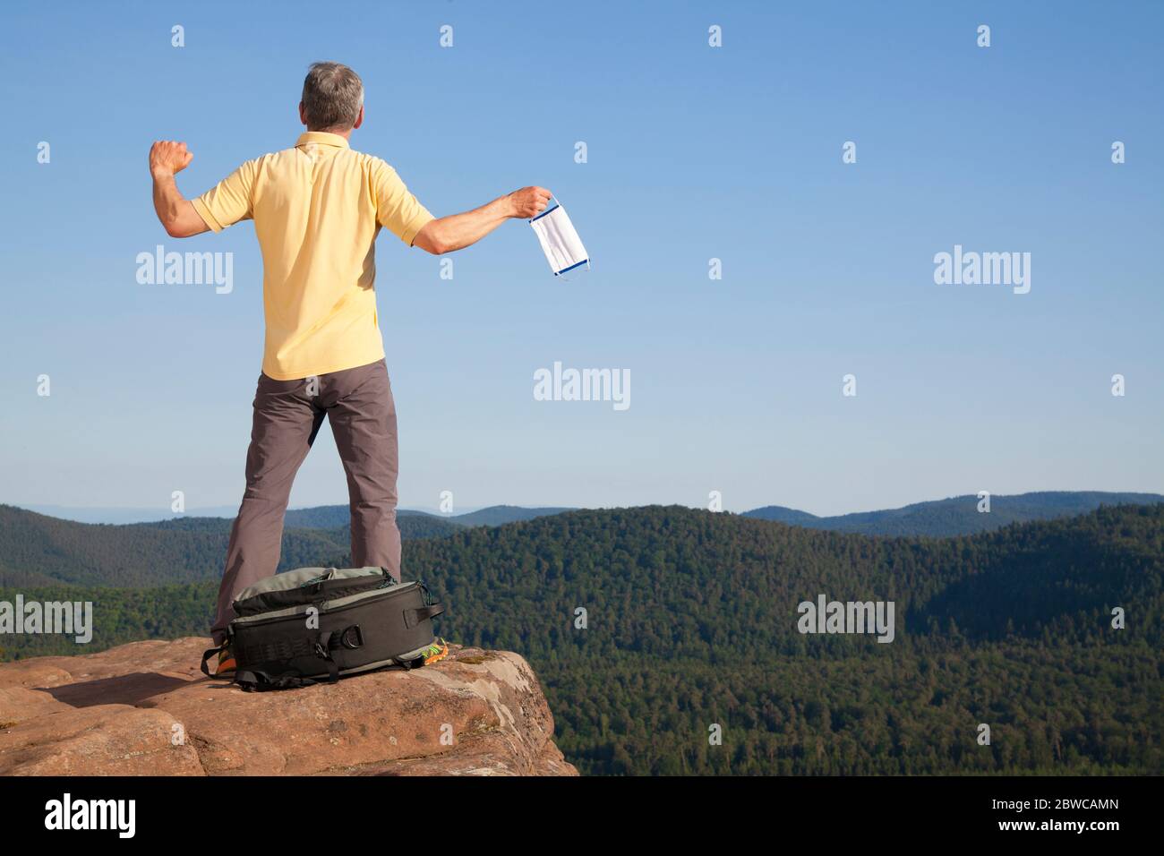 Reifer Mann, der sich auf einem Felsen vor einer Landschaft mit einer Gesichtsmaske in der Hand entspannt Stockfoto