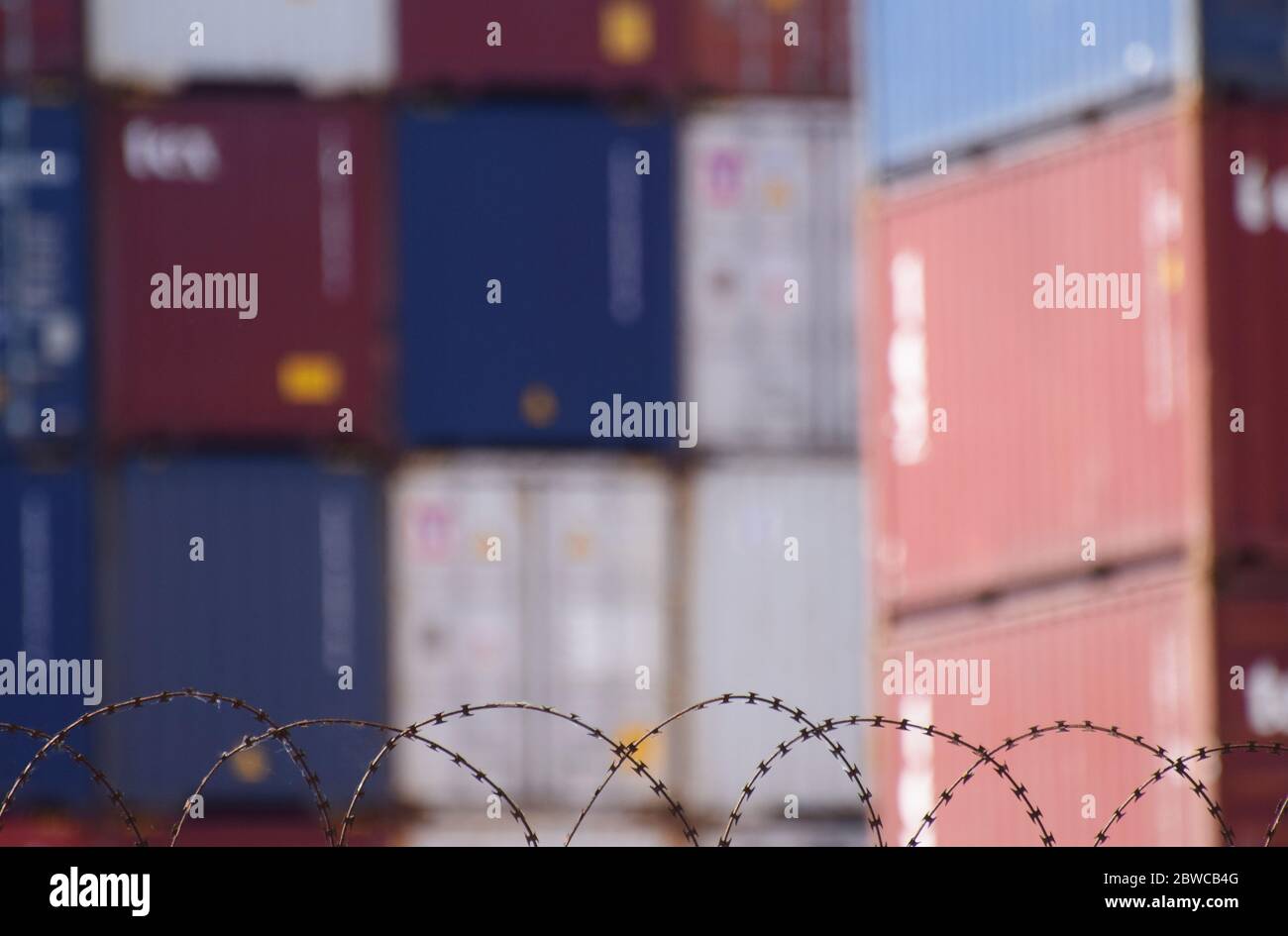 Hinter Stacheldraht stapelte Frachtcontainer an einem belebten europäischen Seehafen Stockfoto