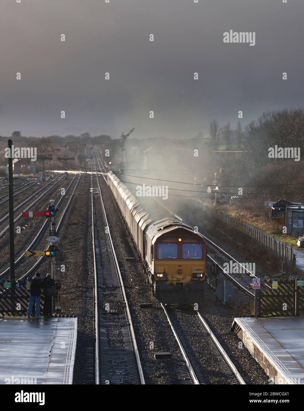 DB Cargo Bahnklasse 66 Lokomotive 66007 vorbei am großen Semaphore-Bracket-Signal in Barnetby, Lincs, mit HTA-Kohlewagen im Sonnenuntergang. Stockfoto