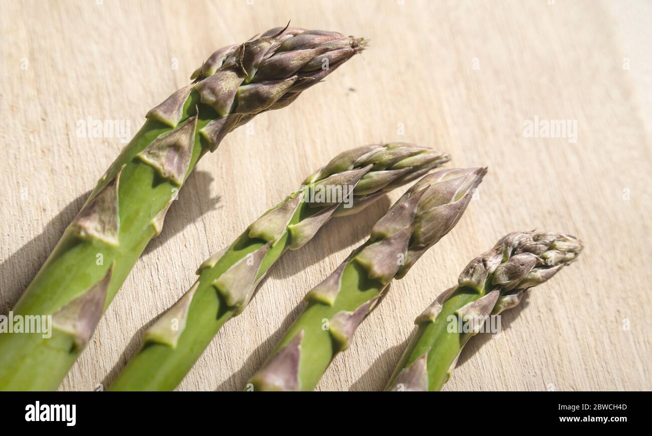 Nahaufnahme von frischen grünen Asparagus Köpfen auf einer hölzernen Küche Boad mit hellem Licht Stockfoto