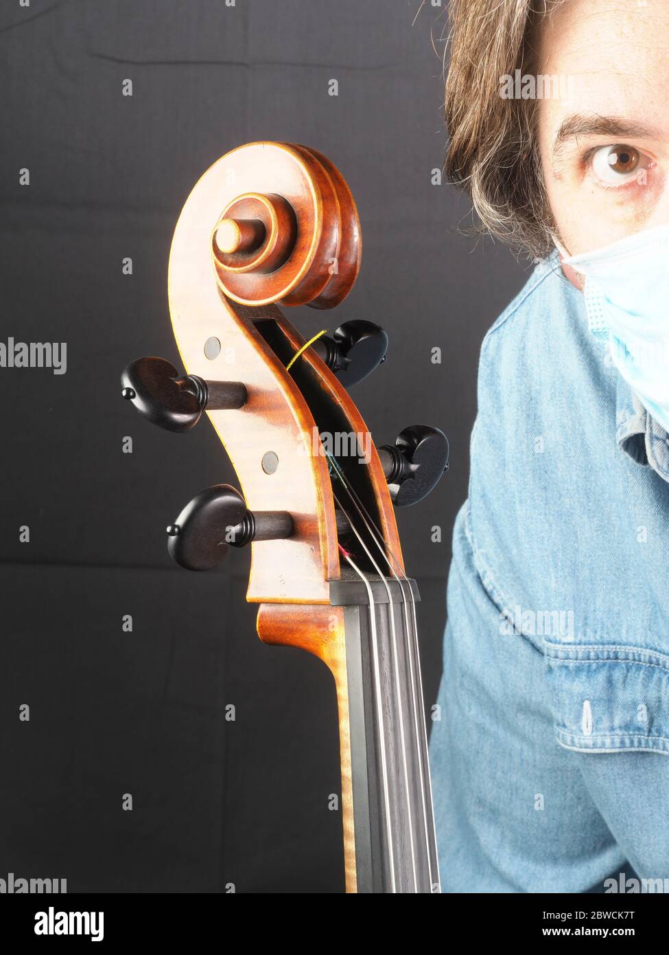 Weißer kaukasischer Erwachsener 50er Jahre Musiker Cellist trägt eine Gesichtsmaske neben einem Cello-Rolle Stockfoto