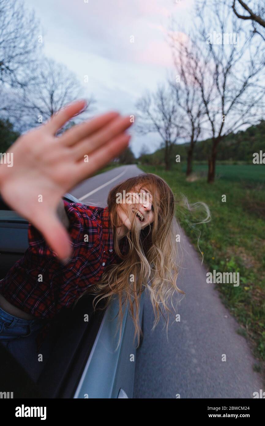 Schöne blonde Mädchen kletterte aus dem Autofenster, sieht und fängt Wind mit seiner Hand. Das Haar flattert. Konzept der Zeit bis zur Reise Stockfoto