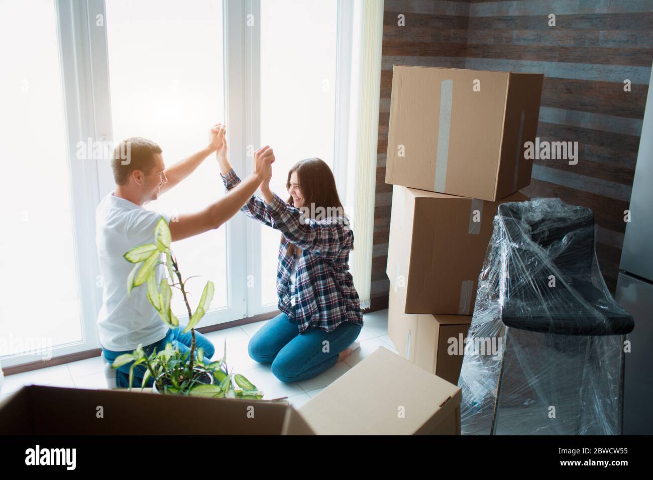 Ein junges Ehepaar im Wohnzimmer im Haus sitzt in der Nähe des Fensters. hey sind glücklich über neues Zuhause. Umzug, Kauf eines Hauses, Wohnung Stockfoto