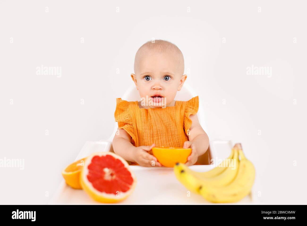 Kleinkind Mädchen sitzt in hohen Kinderstuhl essen Früchte auf einem weißen Hintergrund. Babynahrung Konzept, Raum für Text Stockfoto