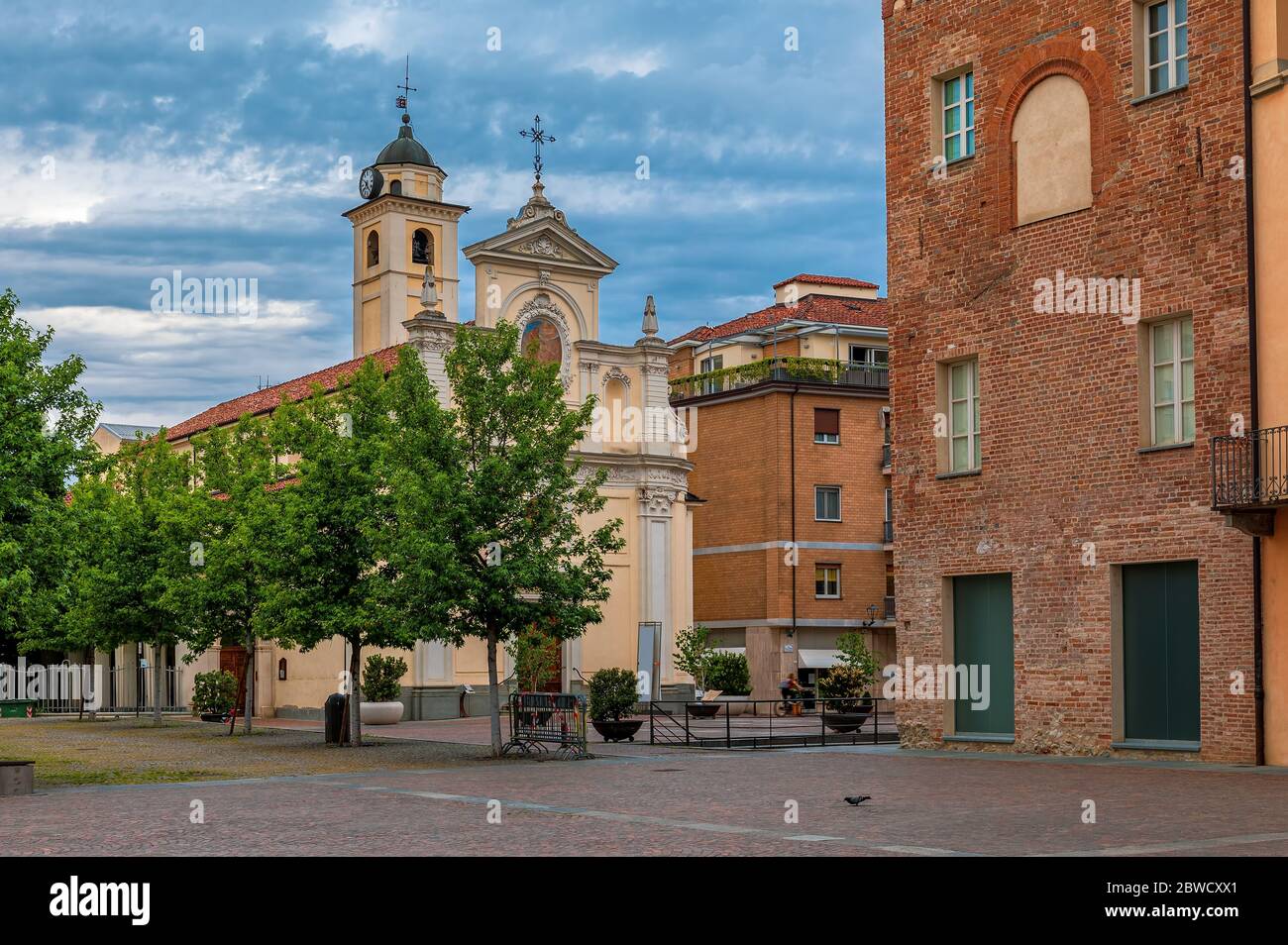 Katholische Kirche auf dem kleinen Stadtplatz unter bewölktem Himmel in Alba, Piemont, Norditalien. Stockfoto
