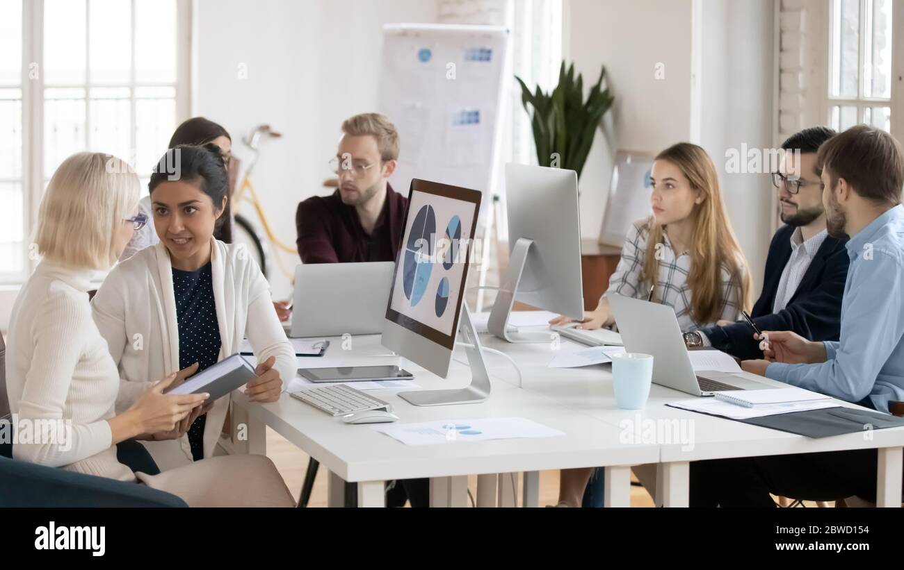 Konzentrierte Kollegen aus gemischten Rennen, die in kleinen Gruppen an Projekten arbeiten. Stockfoto