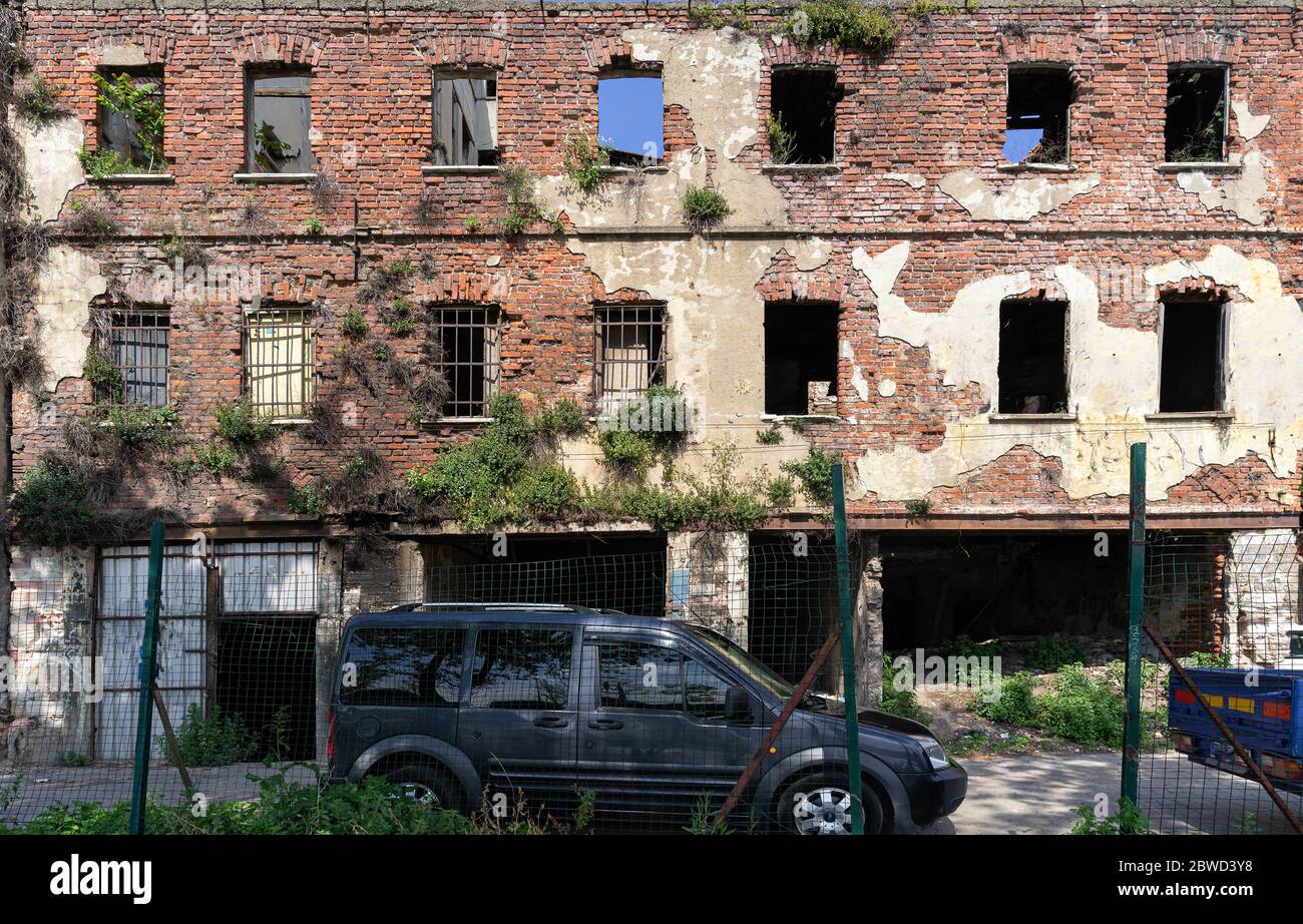 Alte Adandoned Ruine Gebäude Backsteinmauer mit Bäumen auf der Steinmauer und Auto daneben gewachsen Stockfoto