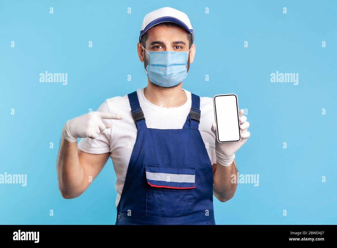Workman in Overalls, Maske und Handschuhe zeigen Handy mit Mock-up leere Display, Werbefläche für Online-Lieferung bestellen App, Haus Reparatur ma Stockfoto