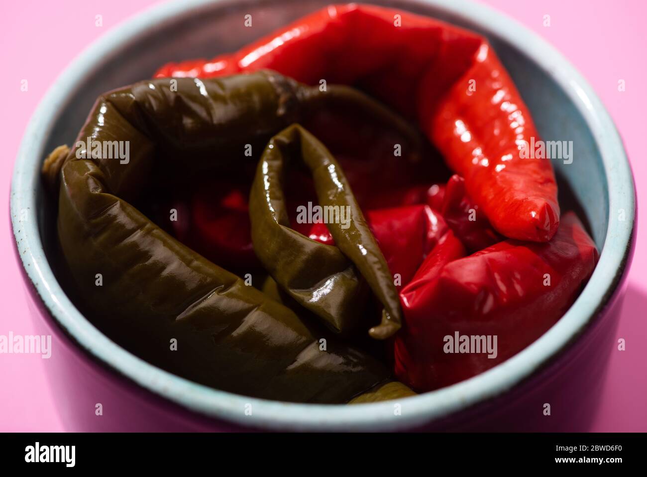 Nahaufnahme von eingelegten Chilischoten in Schale auf rosa Stockfoto