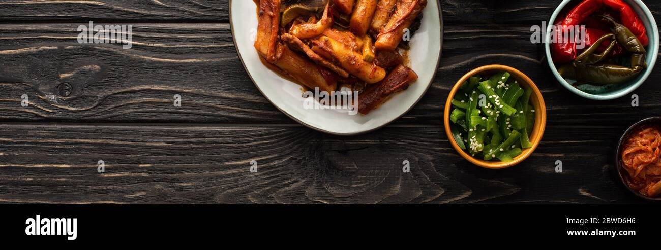 Panoramische Ausrichtung von koreanischem Topokki in der Nähe von Kimchi, eingelegte Chilischoten und grüne Paprika auf Holzfläche Stockfoto