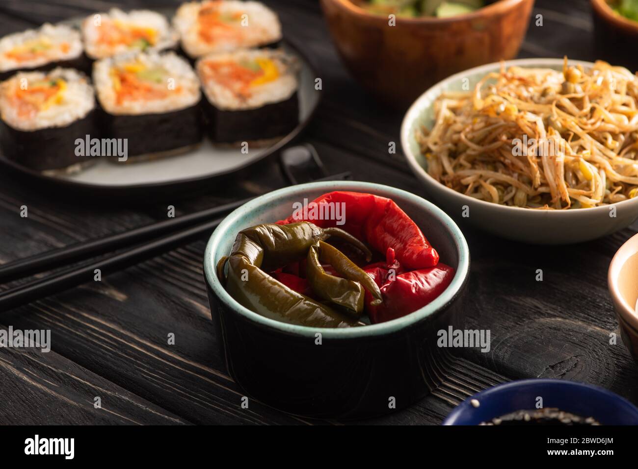Selektiver Fokus von eingelegten Chilischoten in der Nähe von Mungbohnen und koreanischer Kimbap auf Holzfläche Stockfoto