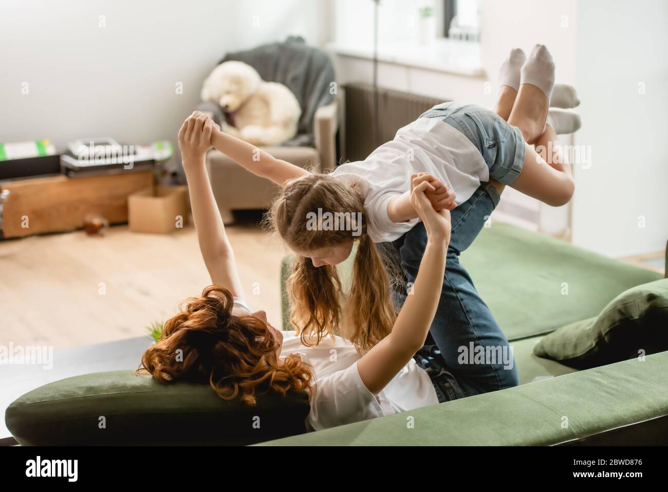 Lockige Mutter liegt auf dem Sofa, Heben niedlichen Kind und hält die Hände im Wohnzimmer Stockfoto