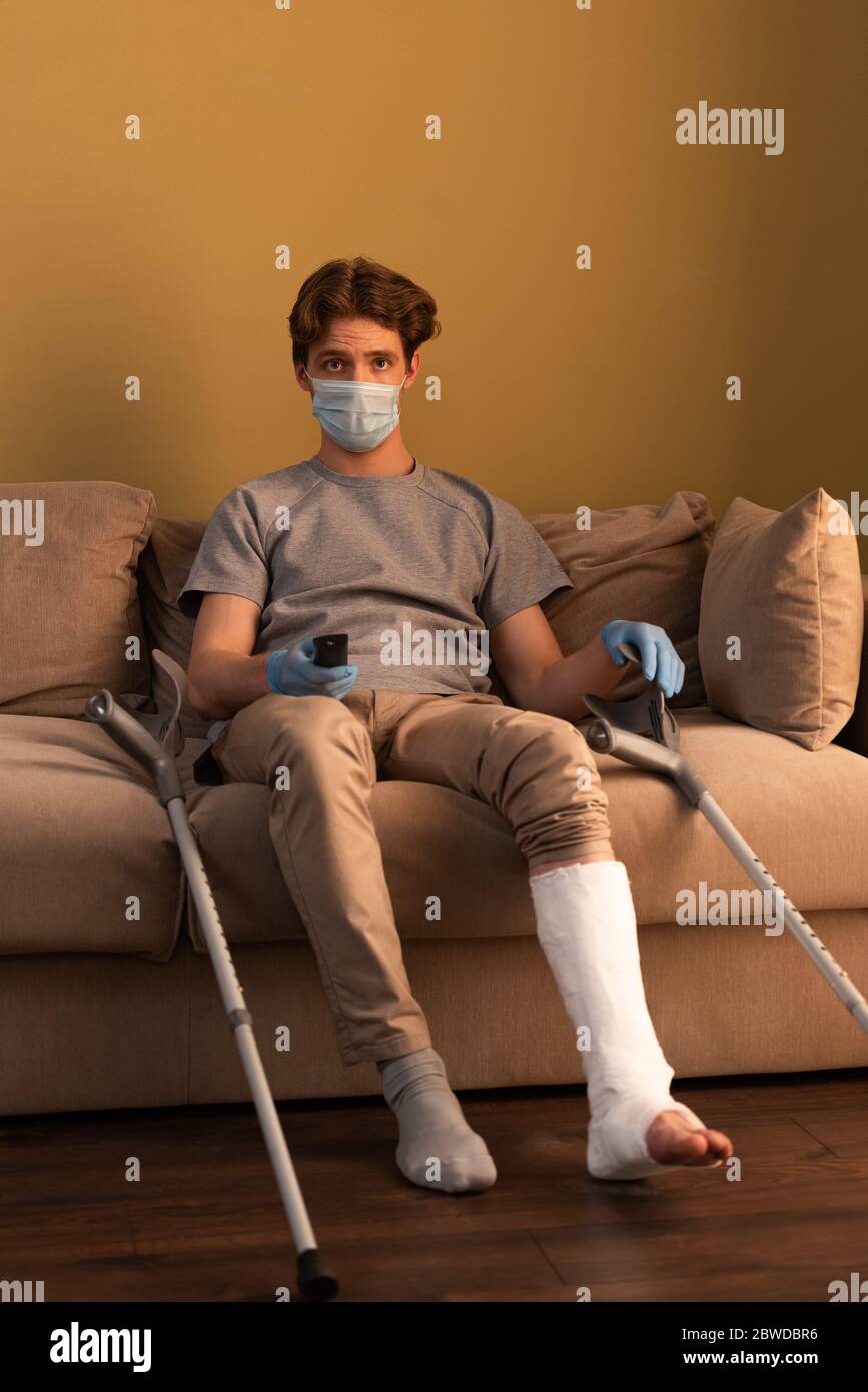 Mann mit in medizinischen Maske und Gipsverband am Bein Fernsehen während  sitzen auf der Couch zu Hause Stockfotografie - Alamy