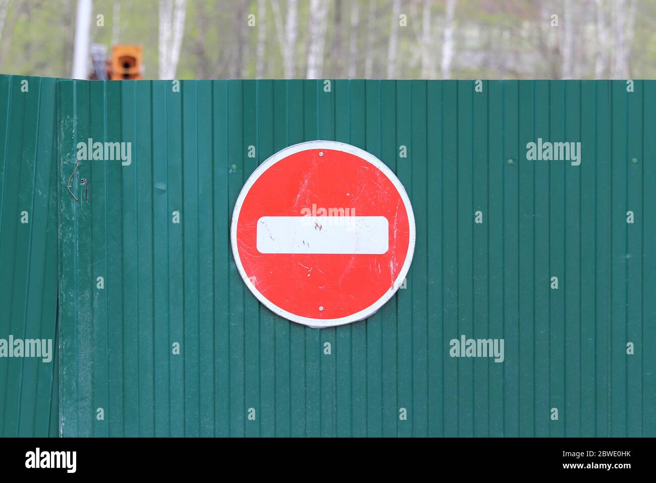 Rotes rundes Straßenschild mit weißem Streifen, das Bewegung auf dem grünen Zaun aus Blech verbietet. Nicht eintreten. Konzept der Prohibition, Sackgasse, Hoffnungslosigkeit und Stopp. Stockfoto