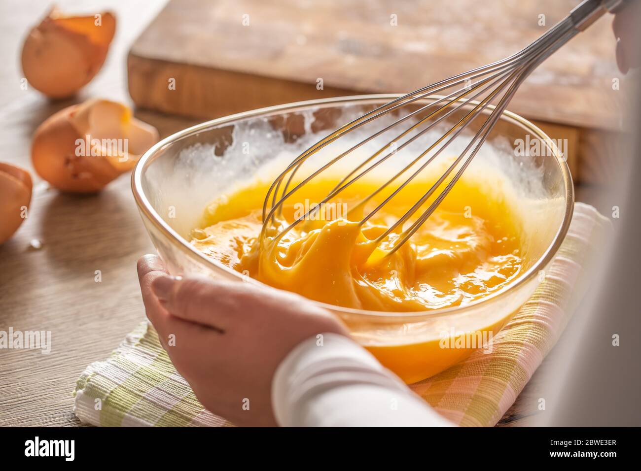 Detail der Eier, die in einer Schüssel auf einem Handtuch und Holztisch gelegt Whisked Stockfoto
