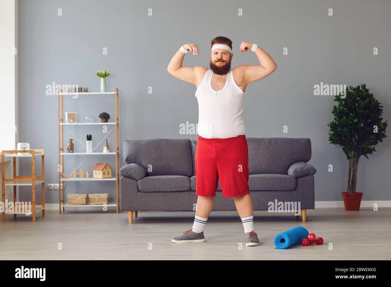 Lustiger fetter Mann in roten Shorts und weißem T-Shirt lächelnd Übungen im Raum machen Stockfoto