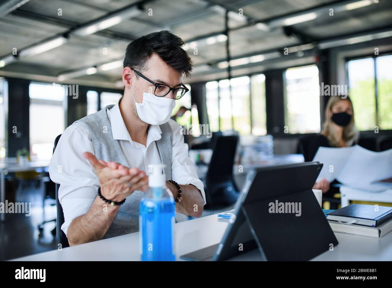 Junge Menschen mit Gesichtsmasken zurück bei der Arbeit im Büro nach dem Lockdown, Desinfektion der Hände. Stockfoto