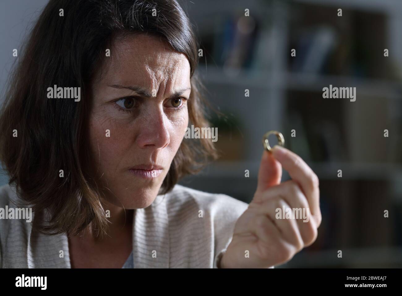 Wütend Frau hält und sieht Ehering sitzen in der Nacht im Wohnzimmer zu Hause Stockfoto