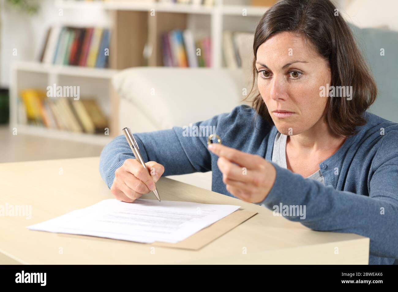 Nachdenkliche Frau Unterzeichnung Scheidung Papiere wegschauen halten Ehering sitzen im Wohnzimmer zu Hause Stockfoto