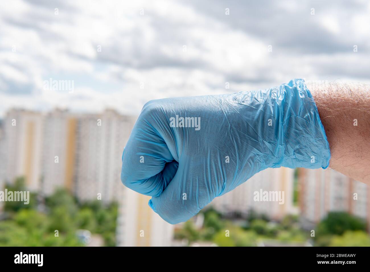 Eine männliche Hand in einem medizinischen Handschuh ballte sich in eine Faust gegen ein Stadtbild Stockfoto