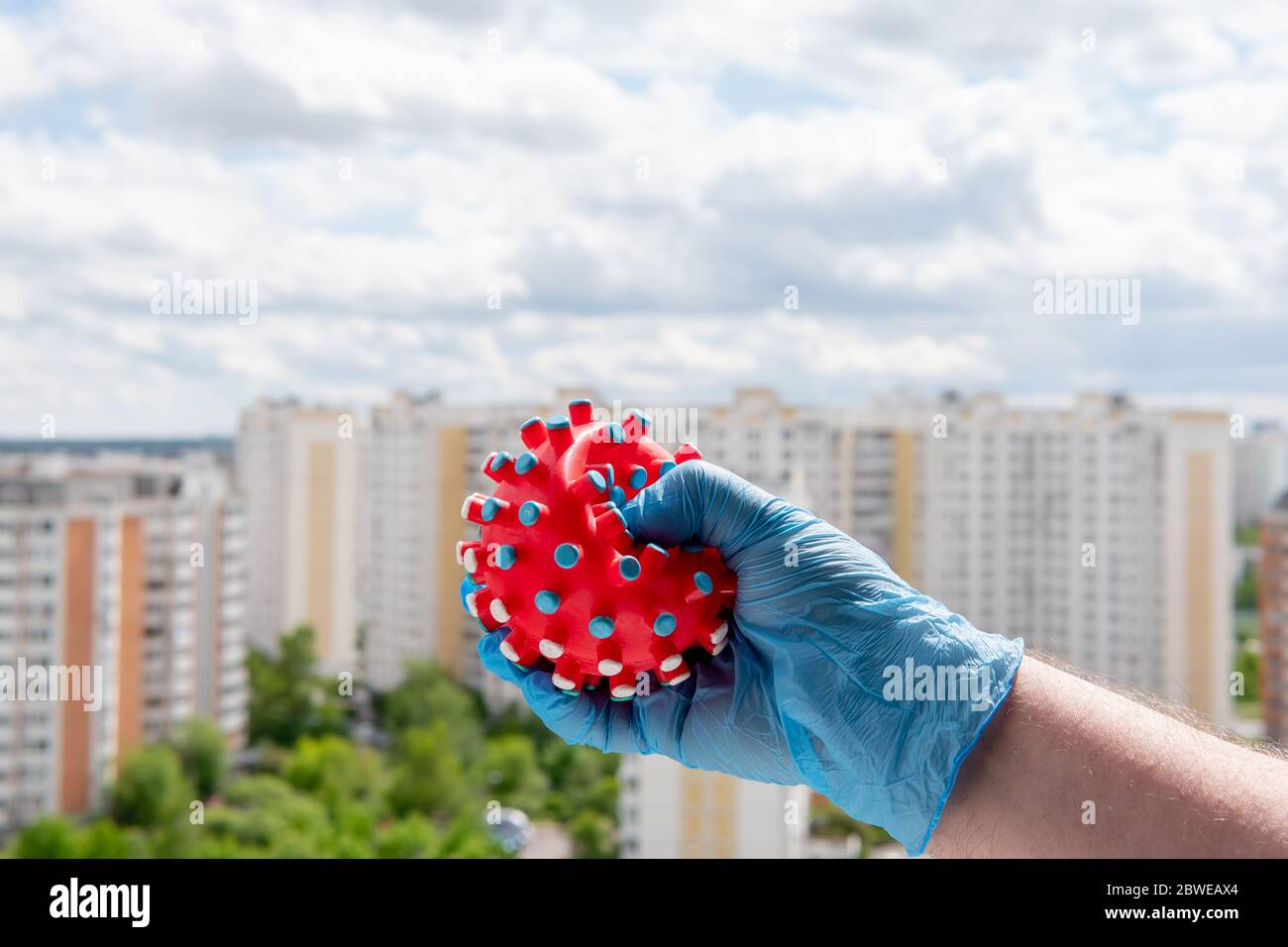Eine männliche Hand in einem medizinischen Handschuh drückt einen symbolischen Virus. Sieg im Kampf gegen Pandemie Covid-19 Stockfoto
