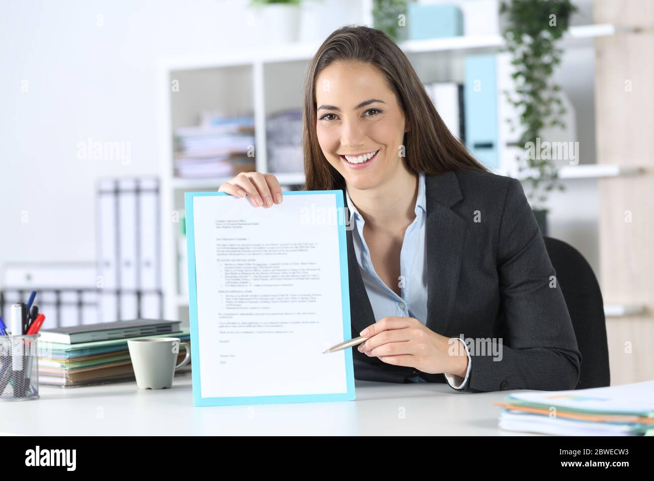 Vorderansicht einer fitschigen Exekutive Frau zeigt Vertrag Unterschrift Raum mit Stift Blick auf Kamera sitzt auf einem Schreibtisch im Büro Stockfoto