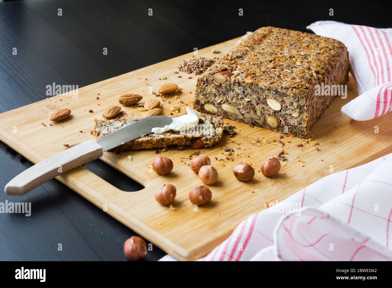 Gesundes selbstgebackenes Keto-Brot mit Mandeln, Haselnüssen, Sonnenblumenkernen, Chiasamen auf einem Holzschneidebrett. Stockfoto