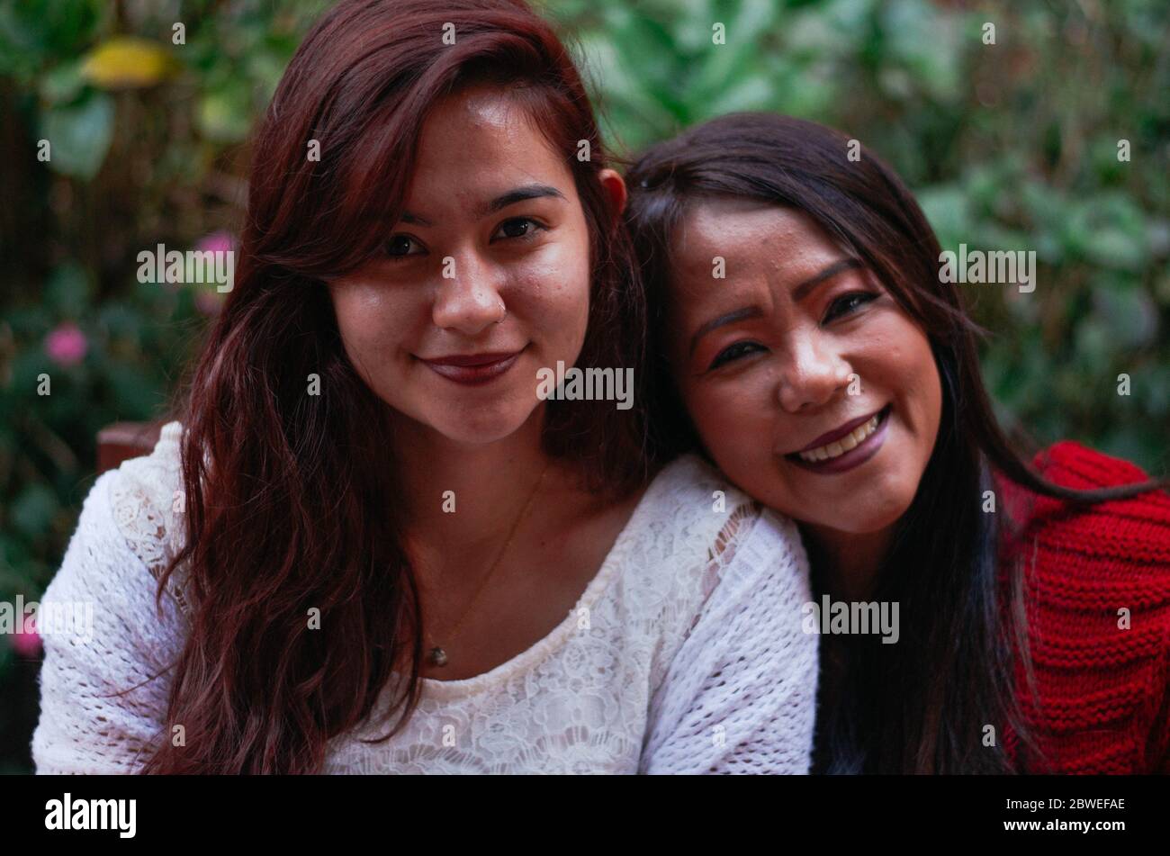 Indonesische Mutter in ihren 50ern und brasilianische Tochter in ihren 20ern lächeln beide in die Kamera. Stockfoto