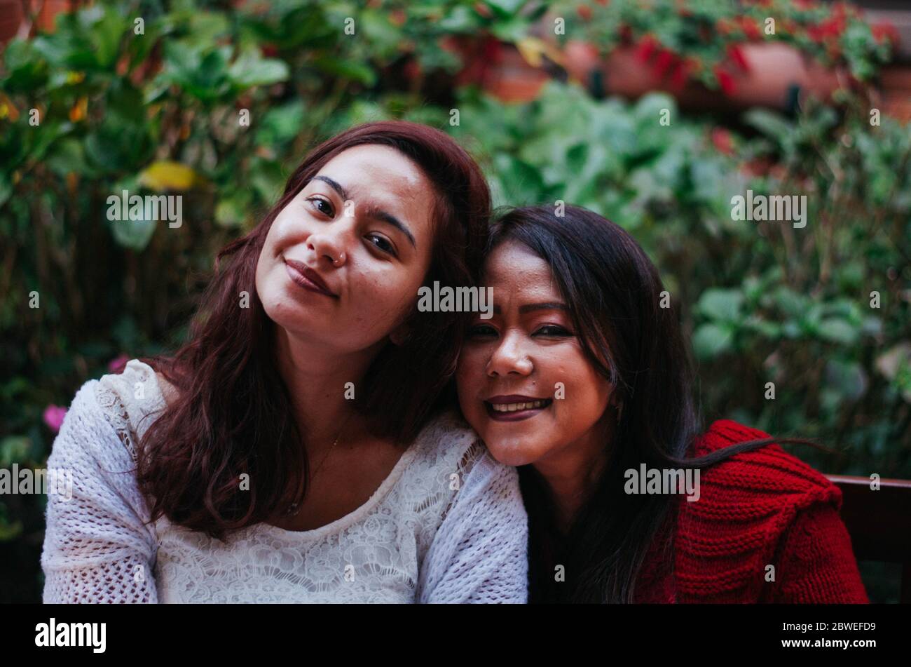 Indonesische Mutter in ihren 50ern und brasilianische Tochter in ihren 20ern lächeln beide in die Kamera. Stockfoto