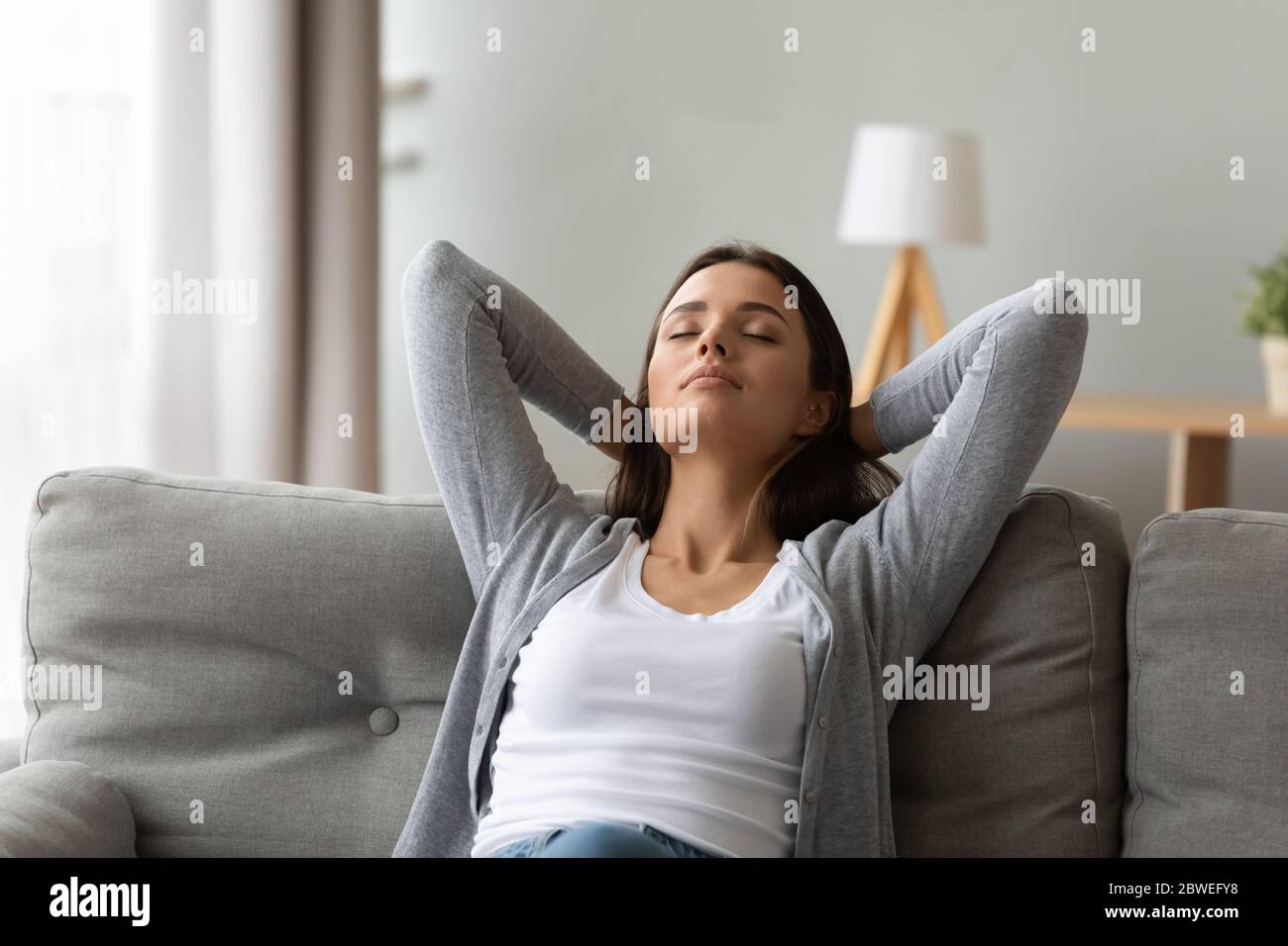 Ruhige Frau legt die Hände hinter den Kopf entspannt auf der Couch sitzen Stockfoto