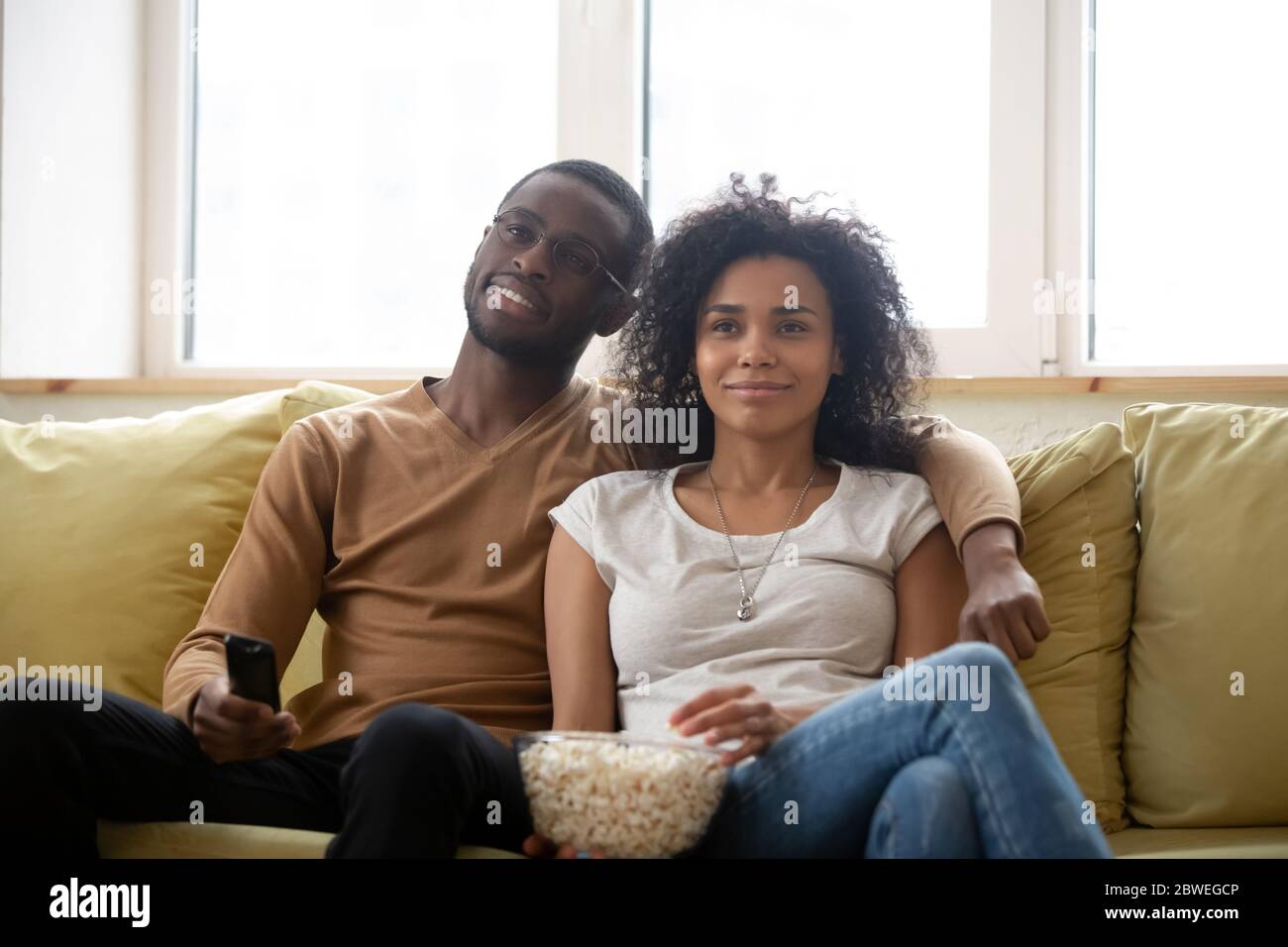 Das Paar sitzt auf der Couch und isst Popcorn und schaut sich Filme im Fernsehen an Stockfoto