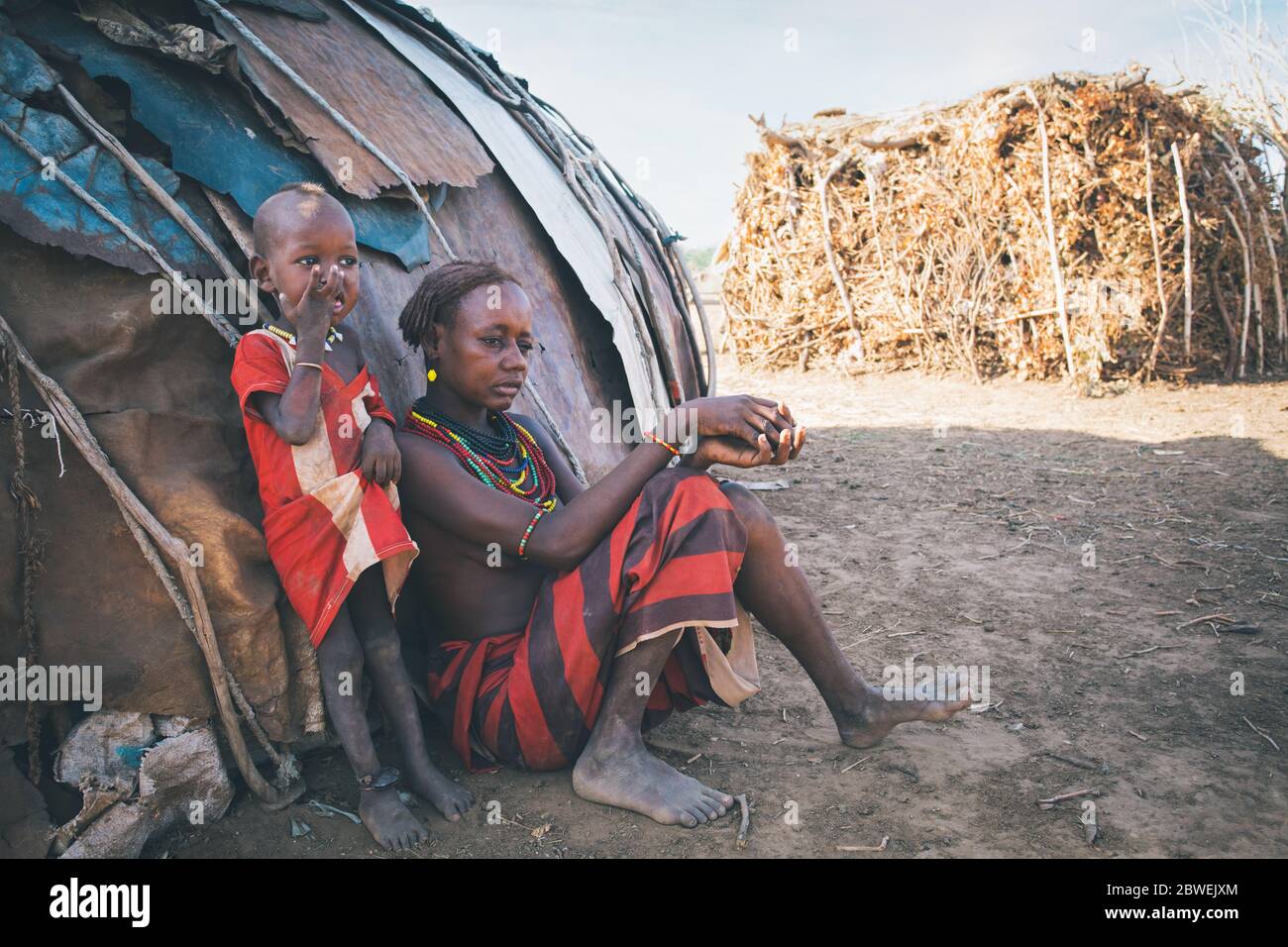 Omorate, Omo Valley, Äthiopien - 11. Mai 2019: Unglückliche Frau aus dem afrikanischen Stamm Dasanesh mit Kind, das im Schatten der Hütte ruht. Daasanach sind Cushiti Stockfoto
