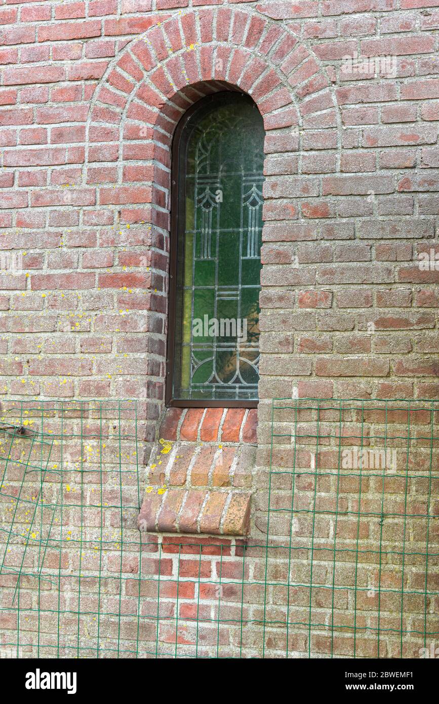 Ovales längliches Buntglasfenster in einer Wand eines Kirchengebäudes mit grün gestrecktem Netz am unteren Rand der Wand Stockfoto