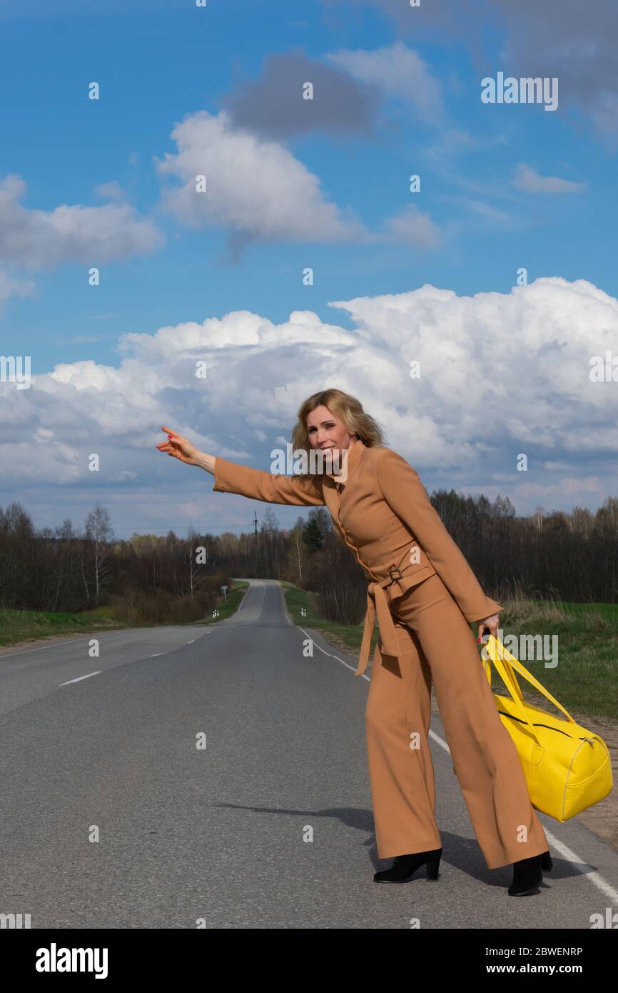 Elegante Frau mittleren Alters in einem modischen Hosenanzug und mit einer gelben Reisetasche in der Hand überquert die Straße. Das Konzept der Erholung von der Stadt und Stockfoto