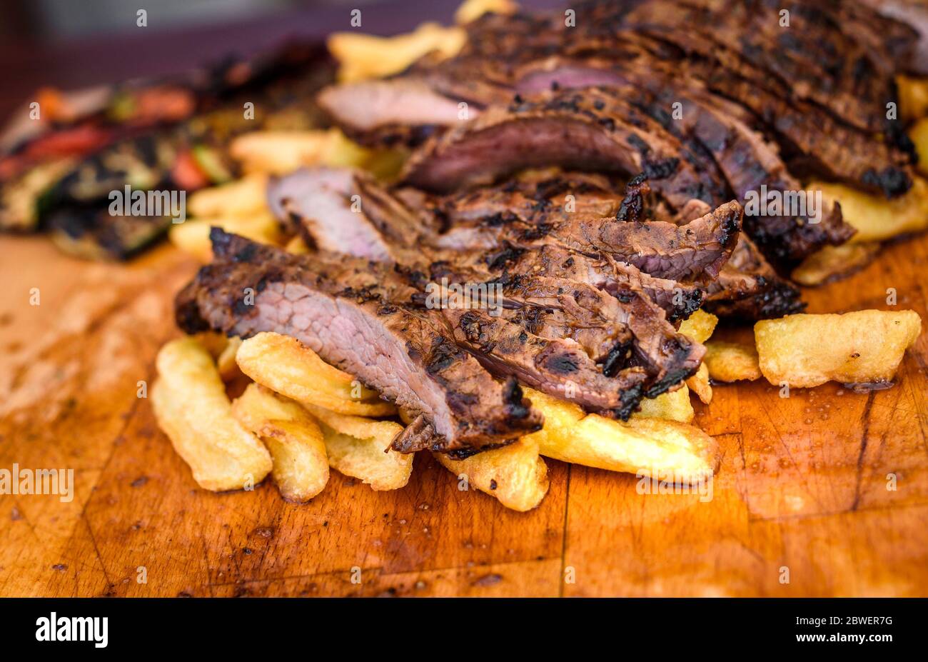 Geschnittenes saftiges vom Grill mariniertes Rindfleisch Flank Steak auf Holzbrett. Saftige medium Fleisch geschnitten und fertig zum Servieren mit Gemüse und gebackene Pota Stockfoto
