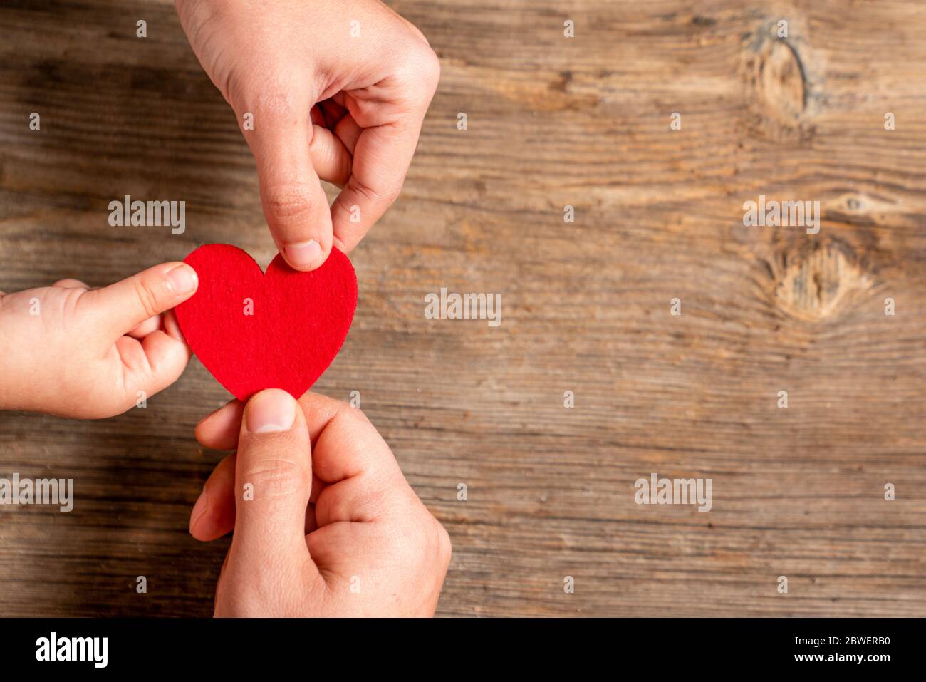 Familienhände mit rotem Herz auf Holzhintergrund. Liebe, Spende, Wohltätigkeit, Gesundheitskonzept Stockfoto