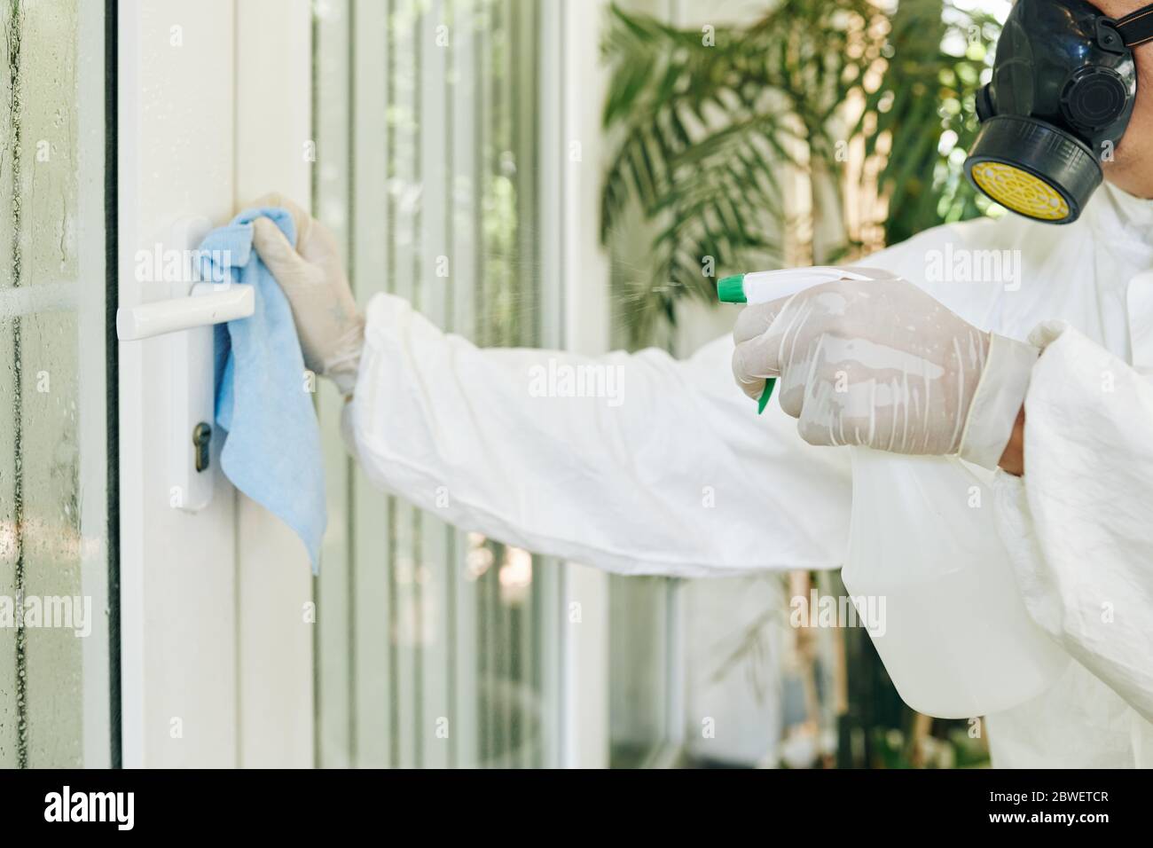 Reinigungsdienstmitarbeiter, die sparsam desinfizieren und Reinigungsmittel am Türgriff verwenden Stockfoto