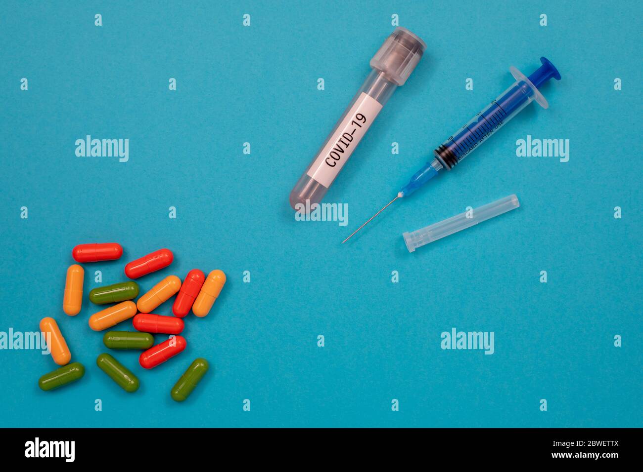 Mehrfarbige Tabletten sind auf dem Tisch, einer Spritze, einer Nadel, einem Reagenzglas verstreut. Draufsicht mit Kopierfläche, flachem Lay. Stockfoto