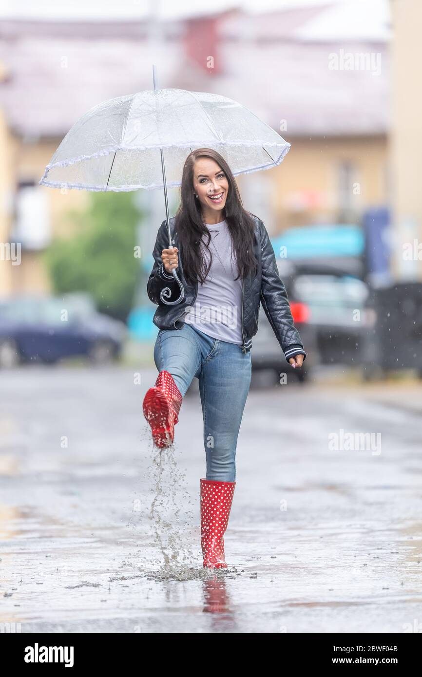 Glückliche Frau in roten Polka Punkt Regenstiefel geht auf der Straße mit einem Regenschirm an einem raidy Tag. Stockfoto