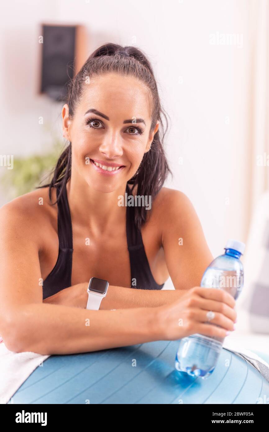 Porträt einer schönen Frau, die sich an beiden Ellbogen auf einen schweizer Ball stützt und eine Flasche Wasser hält. Stockfoto