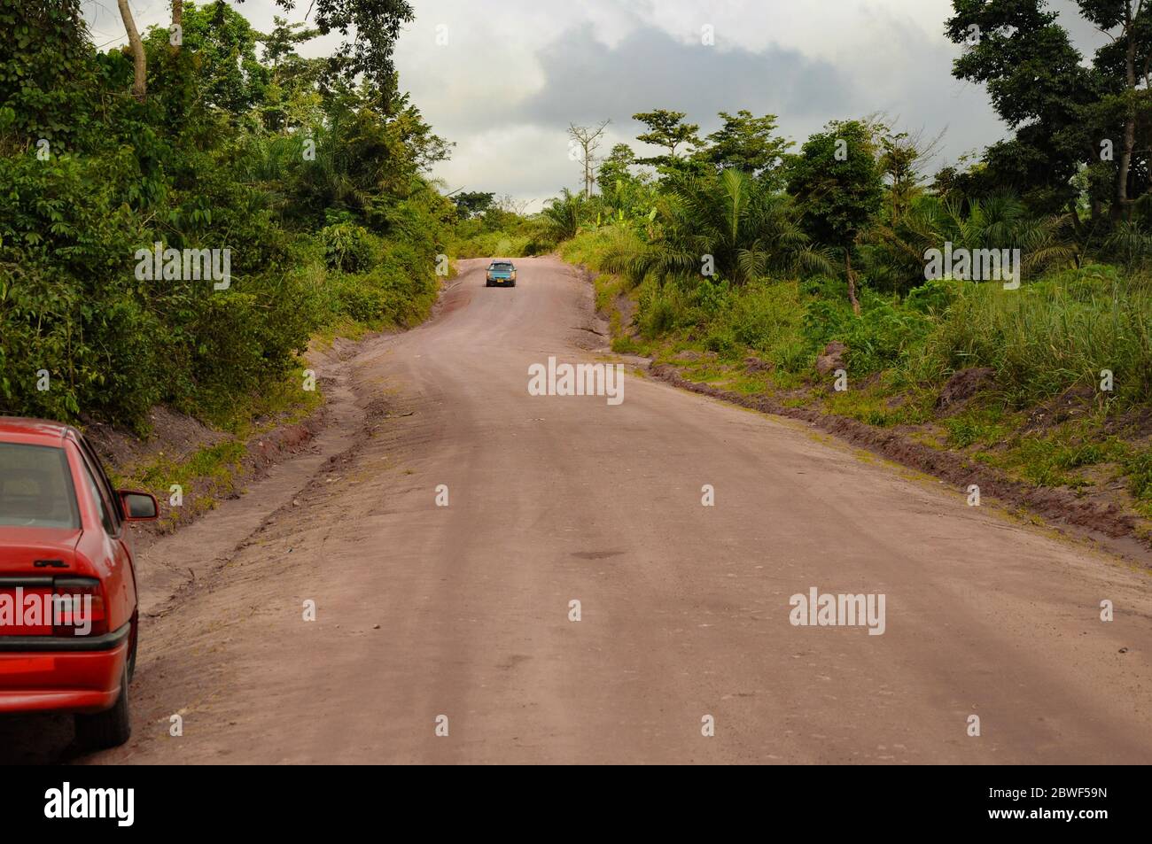 Eine Schotterstraße, die mit einem Auto durch den afrikanischen Regenwald/Dschungel führt - in der Nähe von Accra, Ghana, Afrika Stockfoto