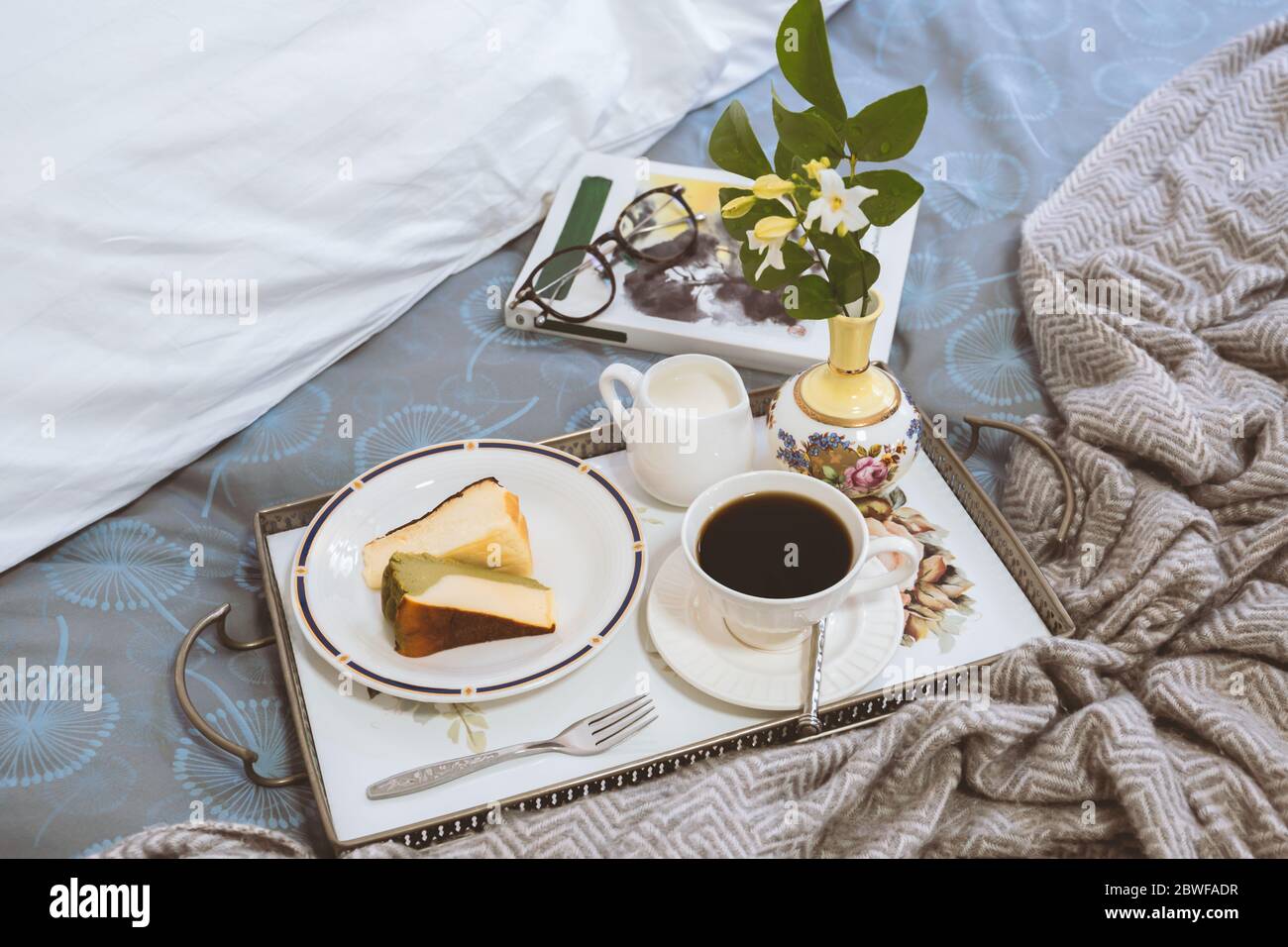 Frühstück im Bett Scheibe Cheesesescake mit Kaffeetasse und Lesebuch. Stockfoto