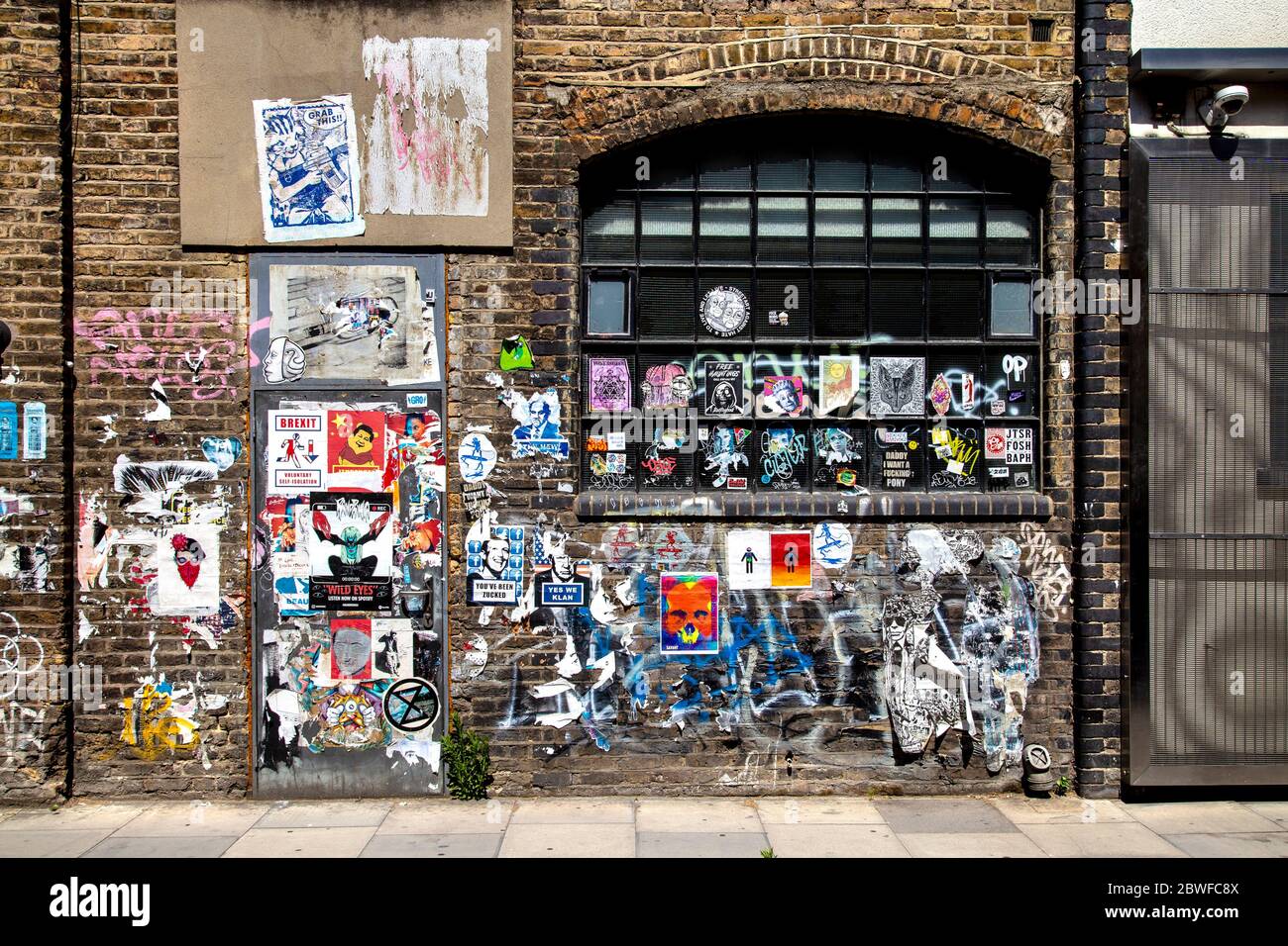 Ziegelwand mit Graffiti, Tags und Plakaten in Fashion Street, Spitalfields, London, Großbritannien Stockfoto